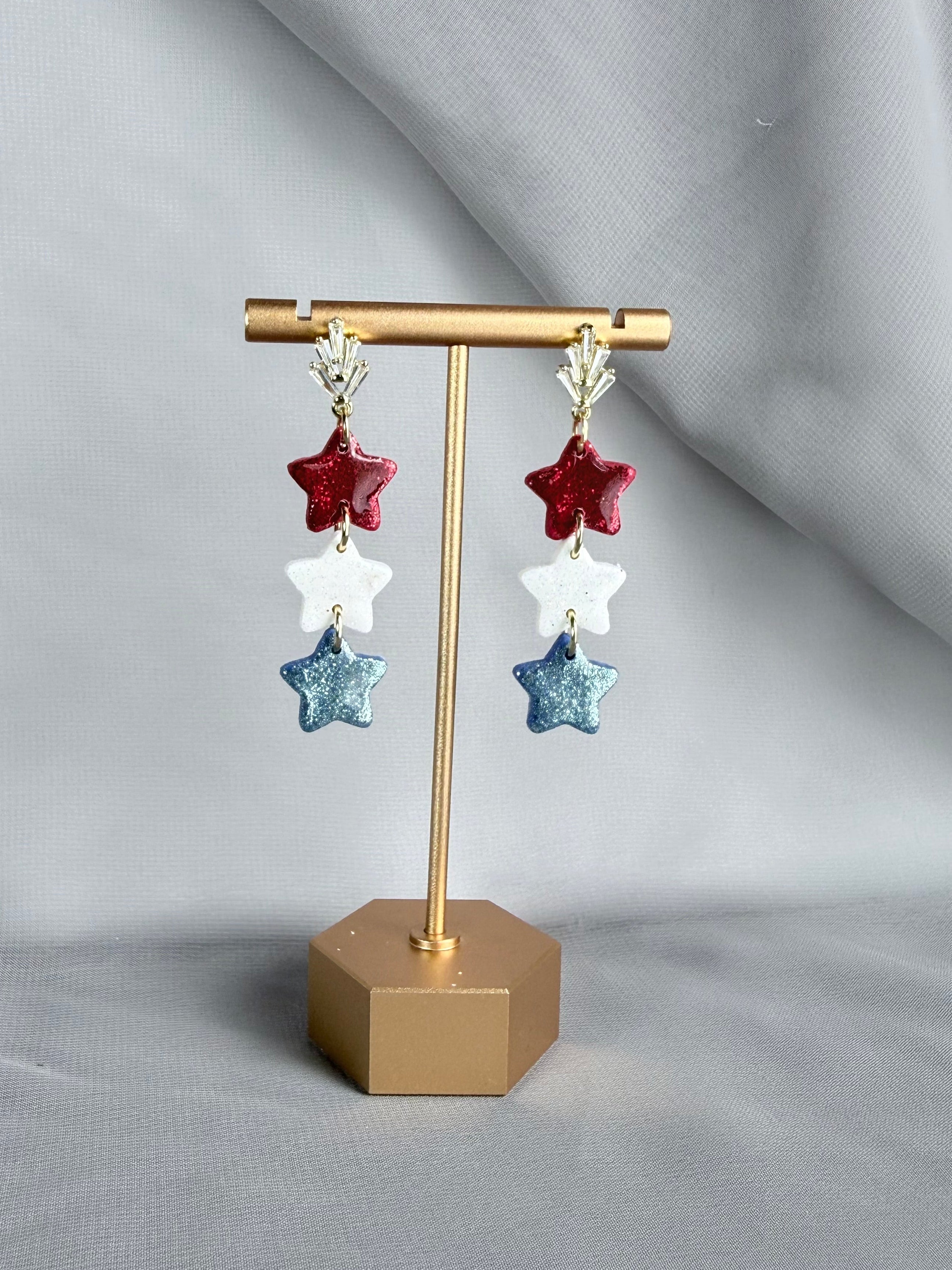 Star-shaped earrings on a gold earring stand against a gray background