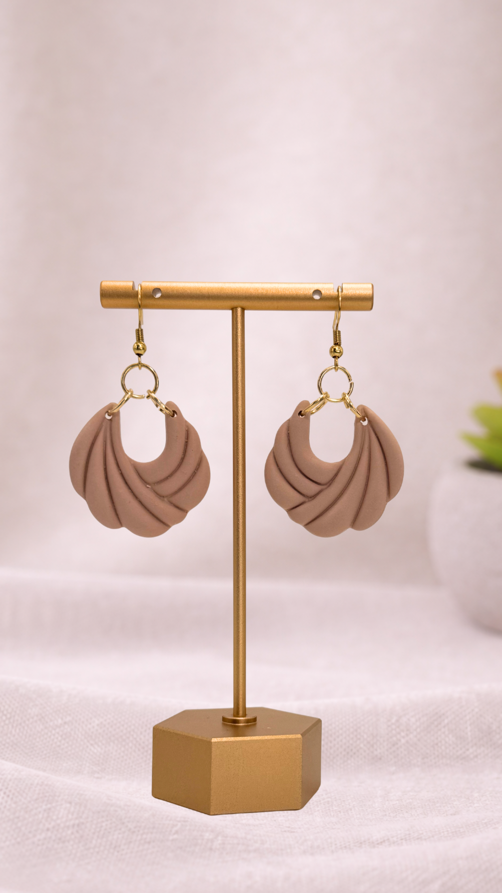 Pair of pink and beige earrings on a gold stand against a light background