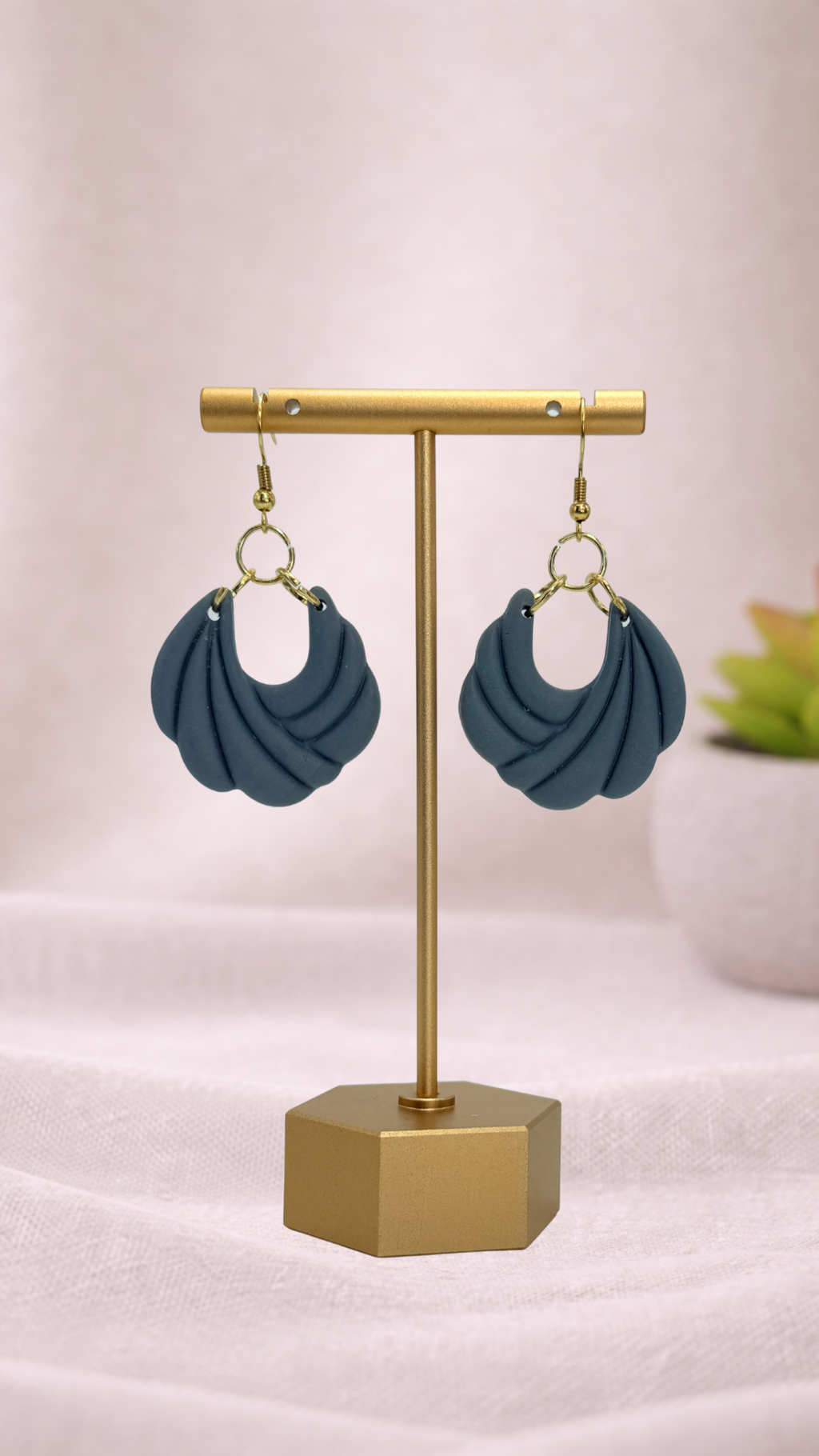 Blue earrings on a gold earring stand with a light pink background